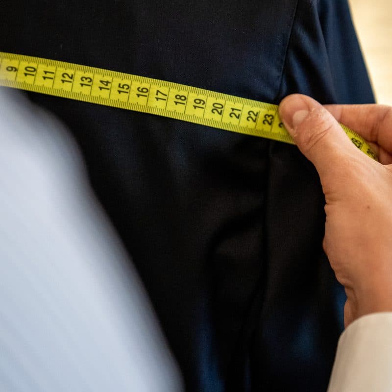 A tape measure checked across the chest of a finished navy jacket before the order leaves the atelier